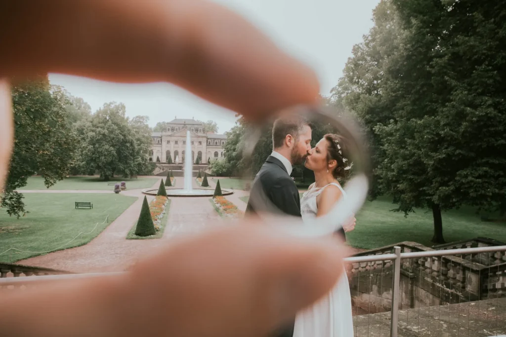 Finger rahmen das Brautpaar vor einem Schlossgarten ein