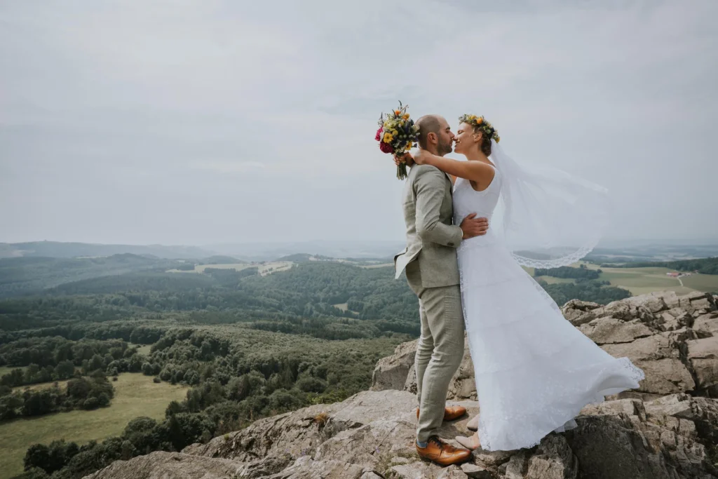 Brautpaar umarmt sich auf einem Felsen über einer weiten Hügellandschaft bei Fulda