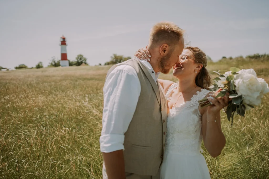 Brautpaar küsst sich auf einer Wiese vor einem Leuchtturm an der Ostsee
