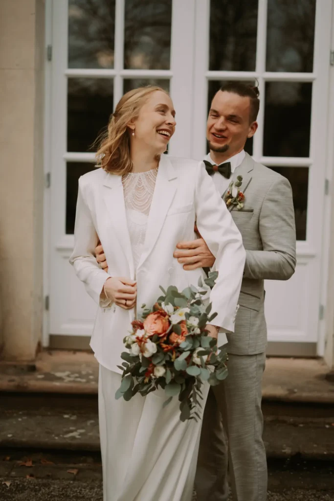 Stella und Alex mit Brautstrauß vor einer weißen Flügeltür