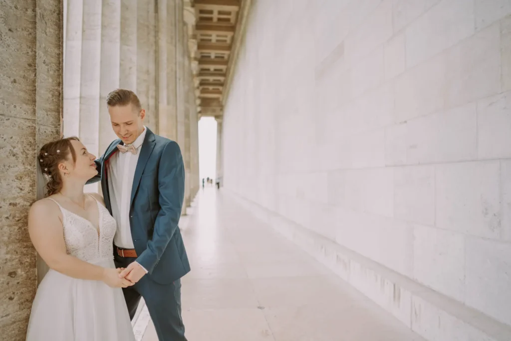 Hochzeit in Regensburg: Braut und Bräutigam lächeln sich an einer Säule der Walhalla an