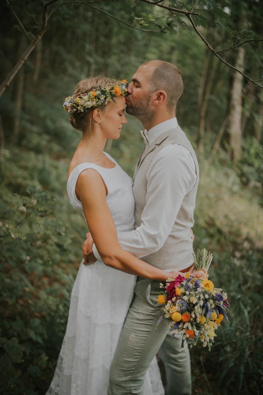 Bräutigam küsst die Braut mit Blumenkranz im Wald am Schloss Fasanerie bei Fulda
